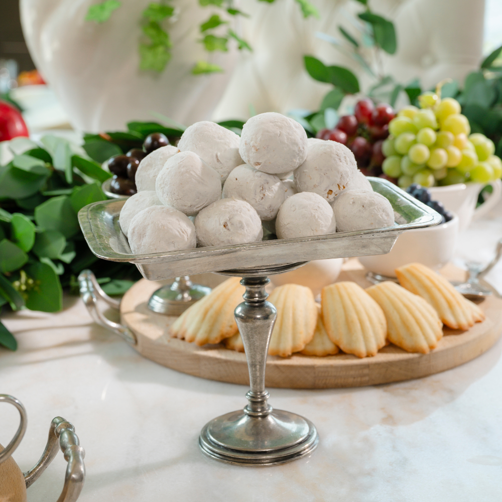 Vintage rectangular pedestal dish piled with powdered donut holes on a marble table with a dessert board