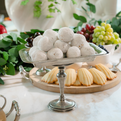 Vintage rectangular pedestal dish piled with powdered donut holes on a marble table with a dessert board