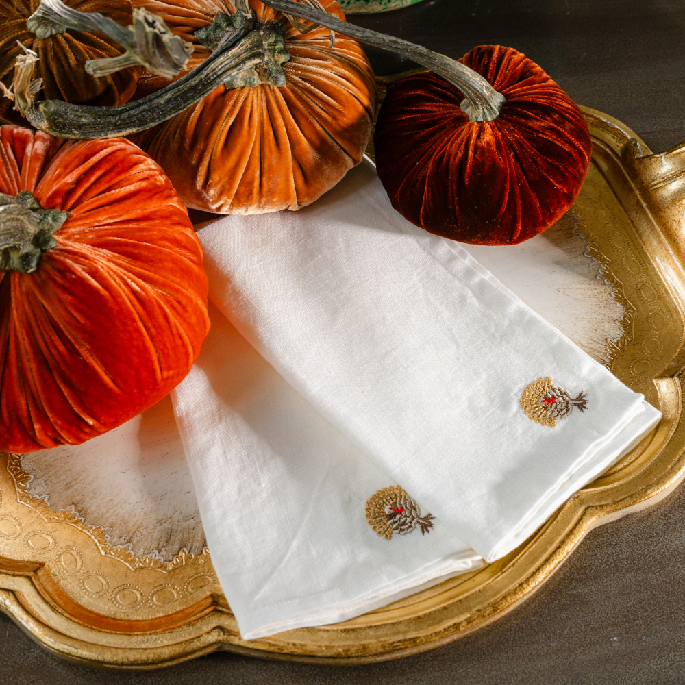 Two washed white linen napkins folded sitting on a gold tray with velvet pumpkins