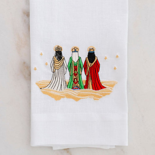 White linen towel with embroidered design of three wise men in colorful robes on a marble surface.