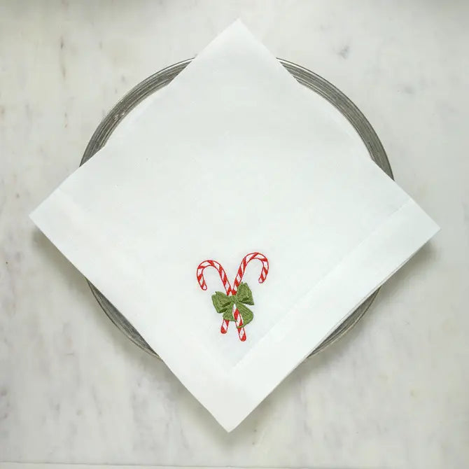 White linen Candy Cane Lane napkin with red and green embroidered candy cane motif, laid flat on a marble surface