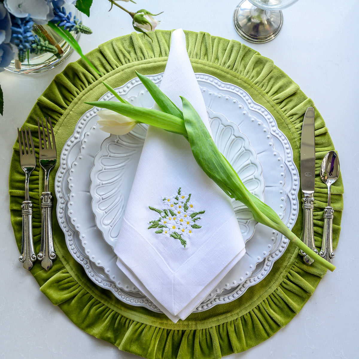 Arte Italica Bella Bianca beaded charger Italian stoneware on green velvet placemat with tulip flower and plate stack
