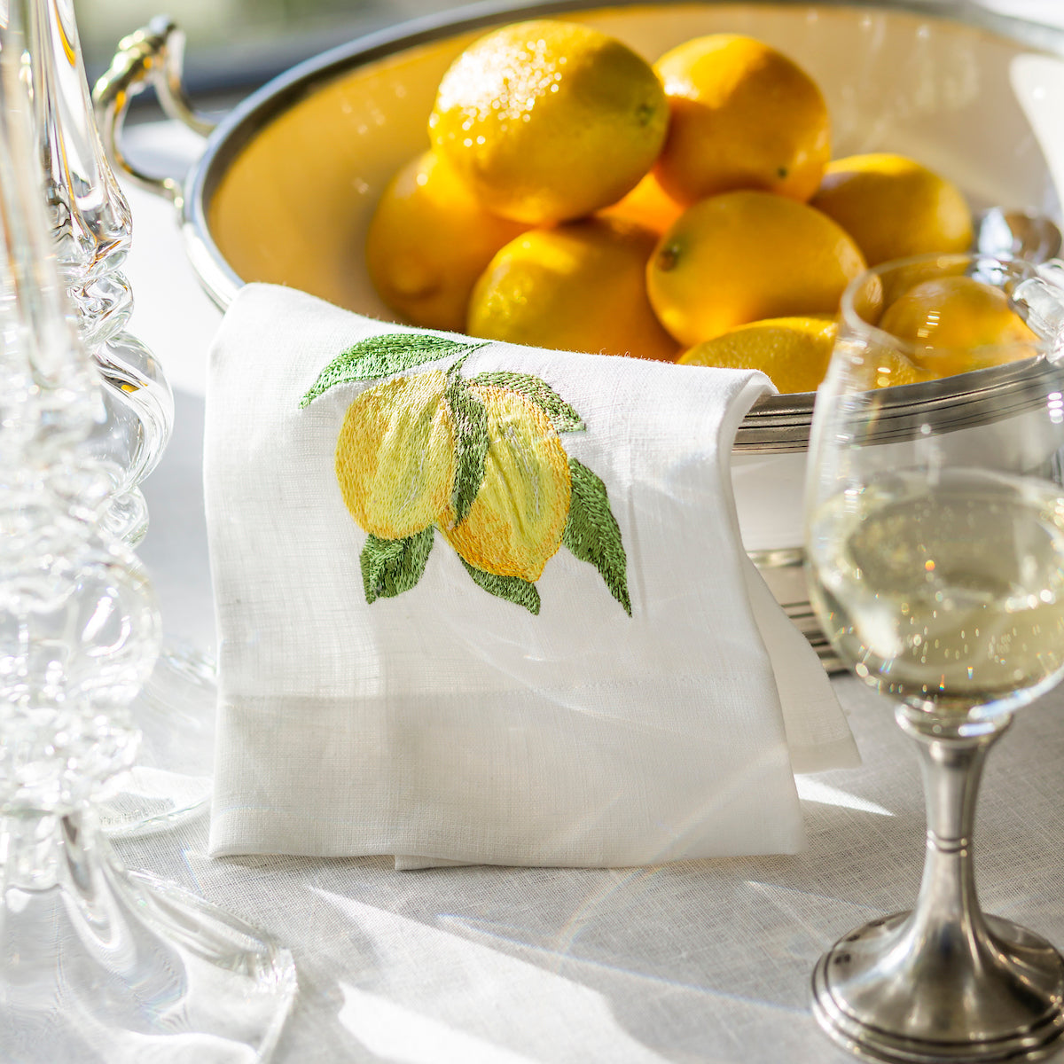 Large Tuscan footed bowl with handles in bianco white ceramic and pewter accents, ideal for serving pasta or salads. Shown with lemons and towel on a table.