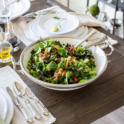 Large Tuscan footed bowl with handles in bianco white ceramic and pewter accents, ideal for serving pasta or salads.  This is shown on table with placesettings.