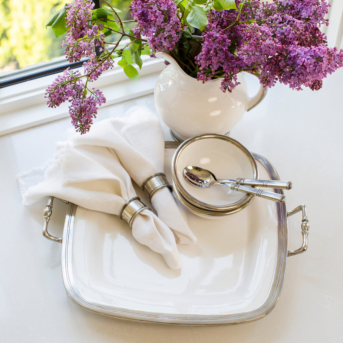 Classic Tuscan rectangular tray with pewter handles and bianco white ceramic base for stylish entertaining. Tuscan Square Tray with Handles with Napkins, Bowls and spoons on a white counter and pitcher with Lilacs