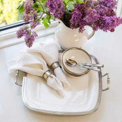 Classic Tuscan rectangular tray with pewter handles and bianco white ceramic base for stylish entertaining. Tuscan Square Tray with Handles with Napkins, Bowls and spoons on a white counter and pitcher with Lilacs