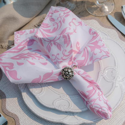 Pink damask Italian cotton napkin in a napkin ring siting on a stack of Bella Bianca plates on a table