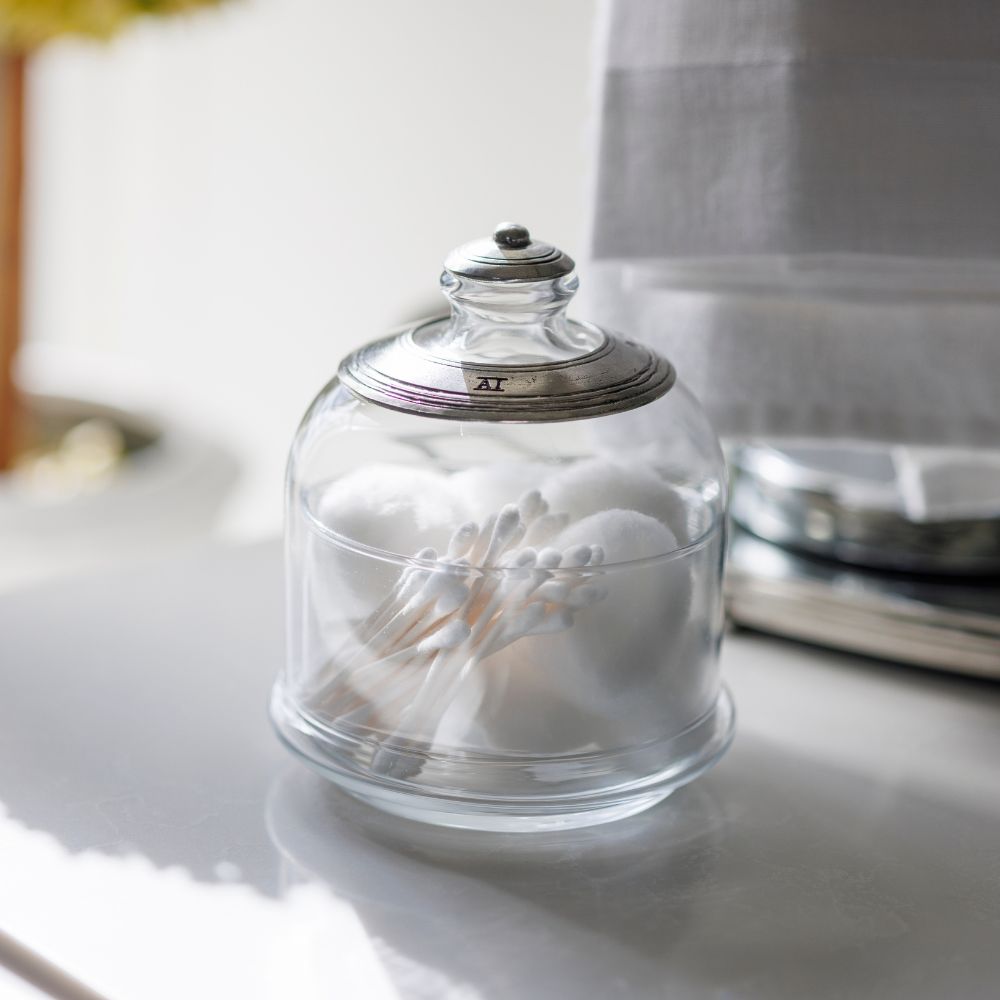 Glass dish with cloche filled with cotton balls and swabs in a bathroom