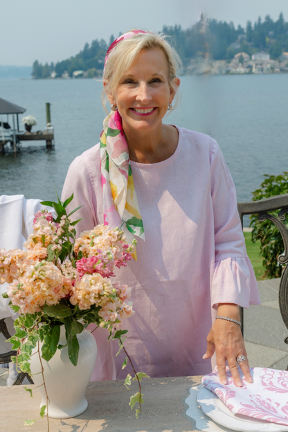 Woman outside wearing the portofino summer garden silk scarf as a headband with a pink bella blouse putting flowers on a table