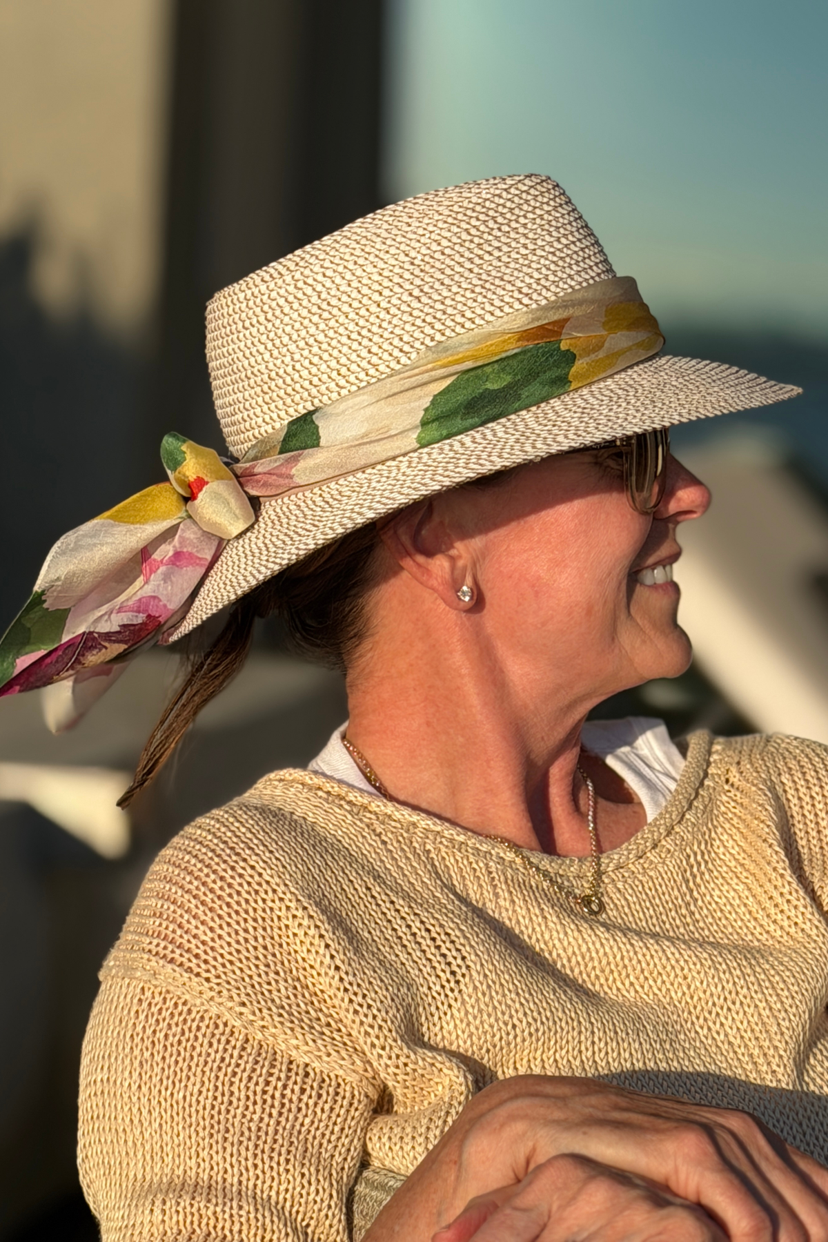 Woman wearing a stylish straw hat the the portofino summer garden silk scarf as a band on her hat with a bow in back sitting outside