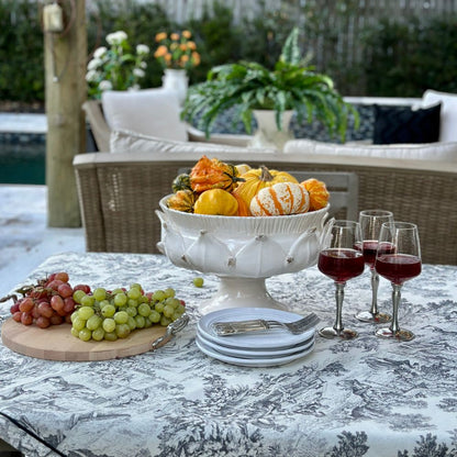 Decorative table setting with an artichoke inspired footed bowl of pumpkins, grapes, and wine glasses outdoors