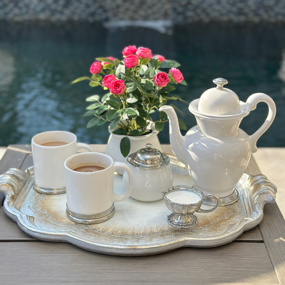 A coffee setting with Tuscan coffee pot and mugs on a florentino wooden tray with a Vintage beaded pewter piccolo creamer with flowers by a pool